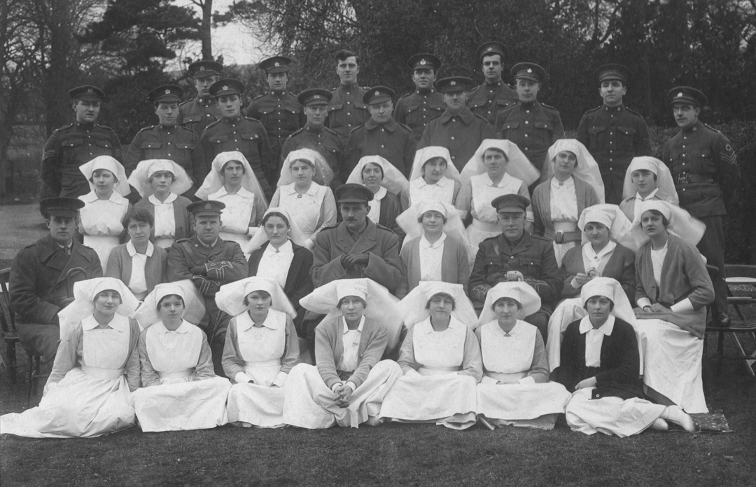 A group of nurses and soldiers pose outdoors for a formal portrait